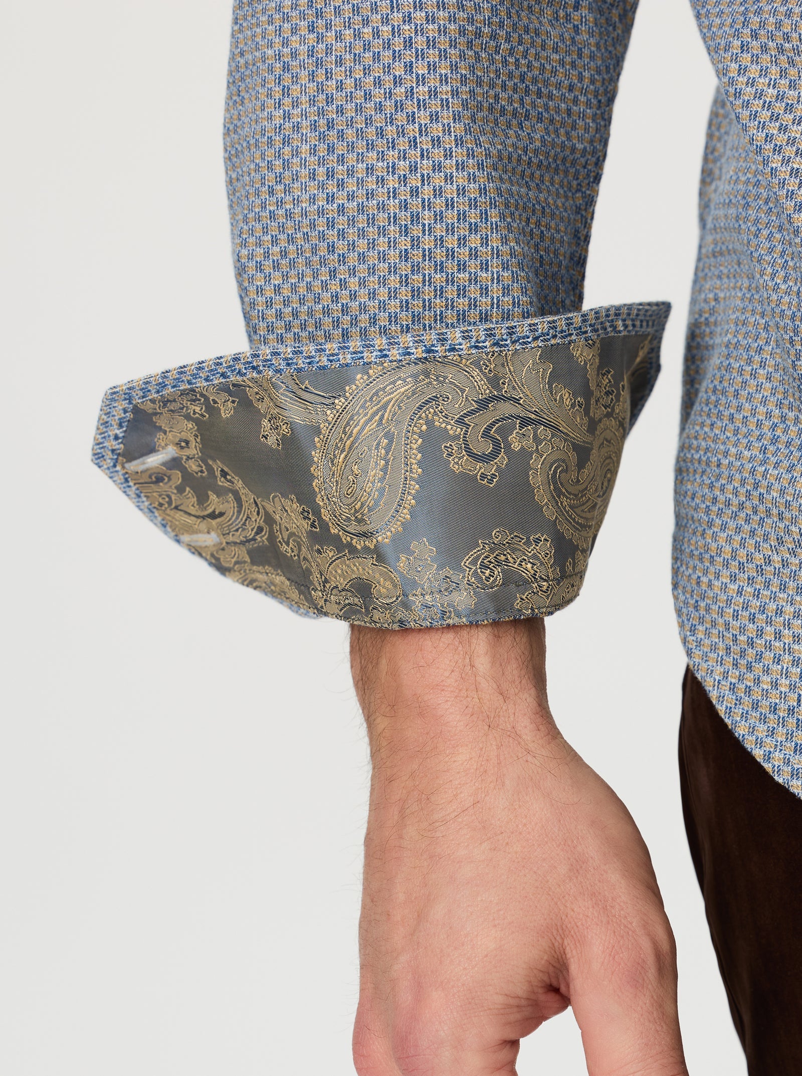 A person wearing the Robert Graham Grandadam Woven Shirt Big & Tall by Robert Graham, featuring a blue cotton micro-check pattern with rolled-up sleeves that reveal a paisley-patterned inner cuff.