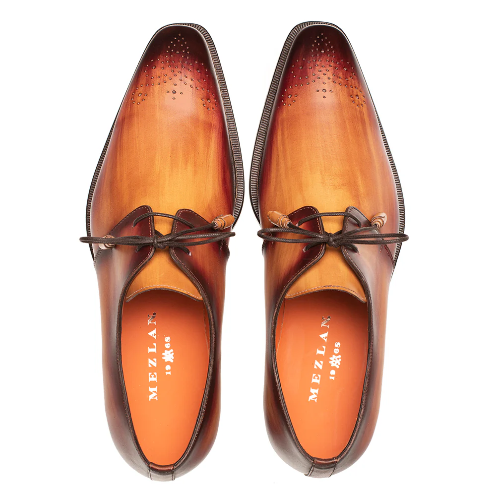 The Mezlan Principe Patina Leather Derby 20842 by Mezlan is a pair of brown Italian calfskin derby shoes with an oxblood gradient finish, laces, and decorative toe perforations, handmade in Spain and shown from a top view.