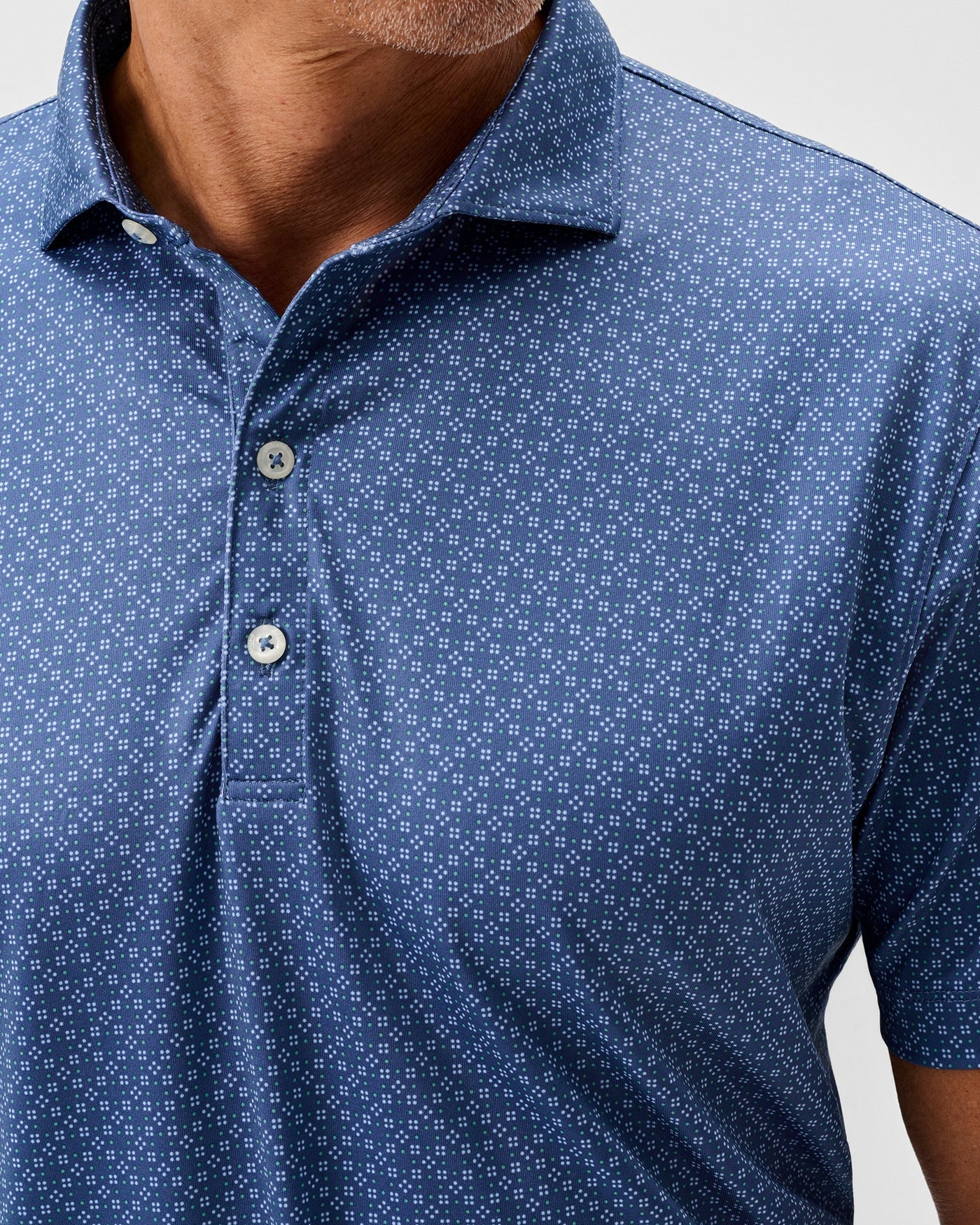 Close-up of a person wearing the Johnnie-O Torres Performance Big & Tall Polo, a blue patterned short sleeve knit button-up shirt with a collar and three white buttons by Johnnie-O.