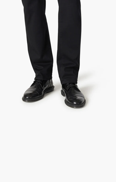 A person wearing 34 Heritage Charisma Double Black pants and black leather dress shoes stands on a white background.