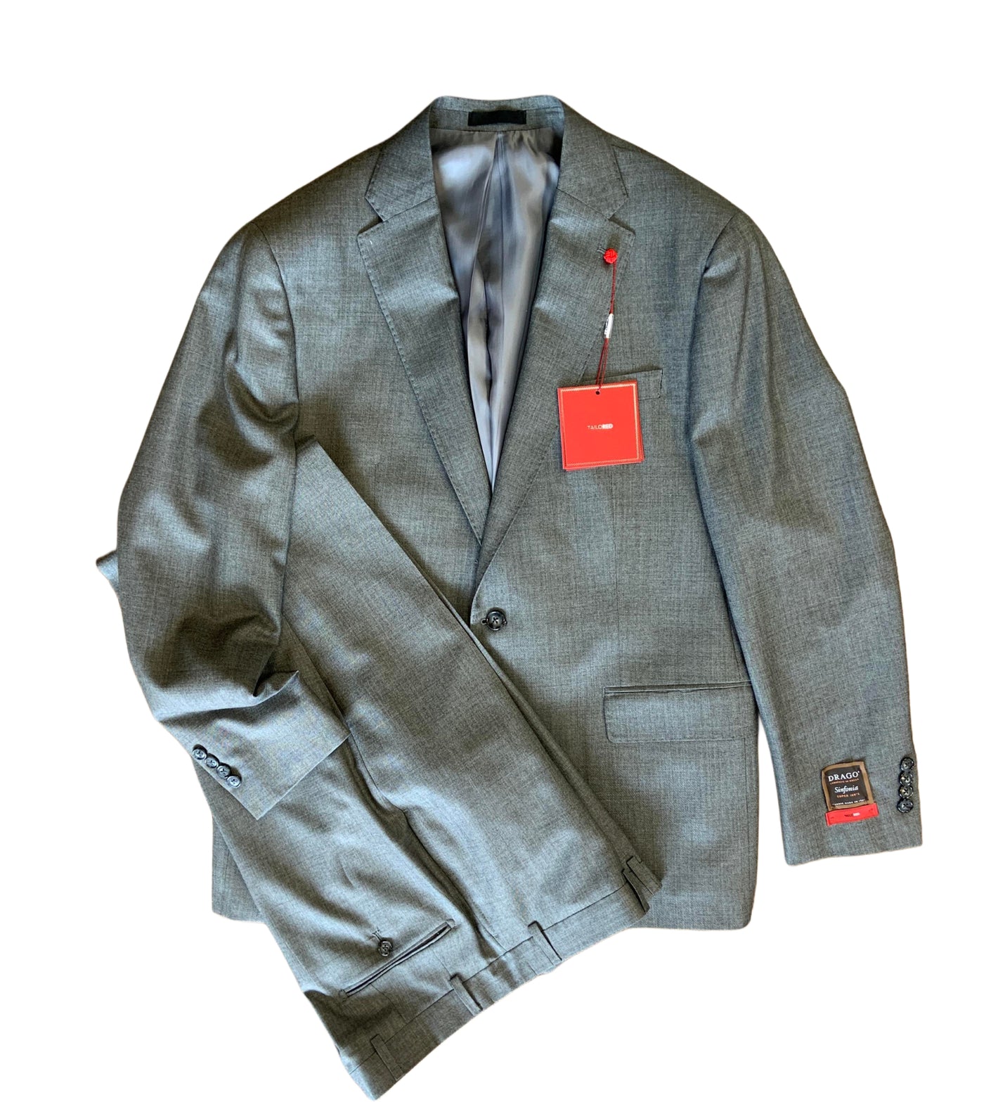 The TailoRed Suit Grenoble 85A0201 is a men’s gray two-piece suit crafted from fine Italian fabrics, featuring a single-breasted blazer with hand-finished details, matching trousers, and tags attached to the jacket.